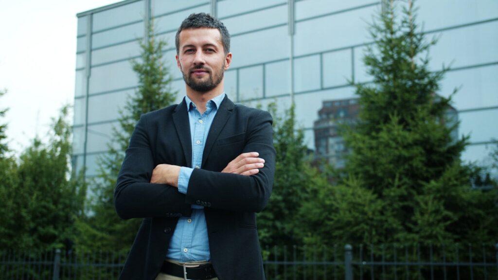 Man in suit standing with arms crossed outdoors.